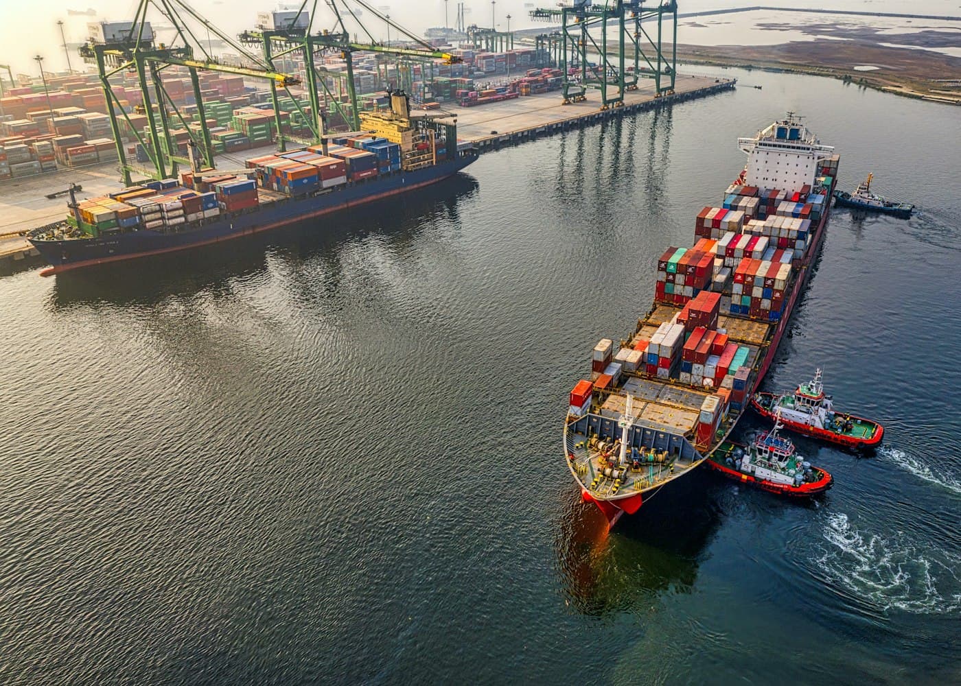 Vista aérea de navio porta-contêineres manobrado por rebocadores em terminal portuário